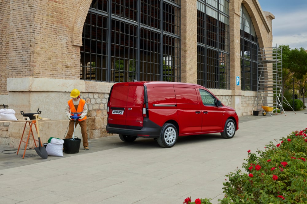 Ford Transit Connect s chromovanými exteriérovými mlhovými světlomety a automatickými světlomety projíždí městem.
