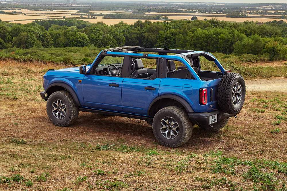 Modrý Ford Bronco s odnímatelnou střechou a dveřmi, zaparkovaný na prašné terénní cestě.