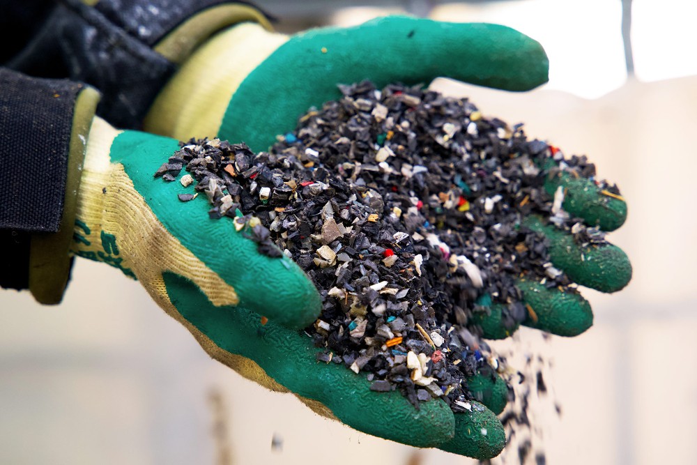 Ruce v gumových rukavicích držící kusy recyklovaného plastového odpadu.