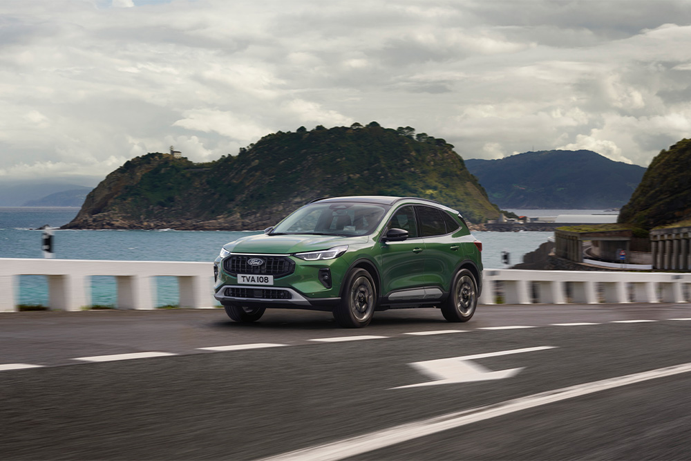 Zelený samonabíjecí hybridní vůz Ford Kuga jedoucí po vyhlídkové silnici.