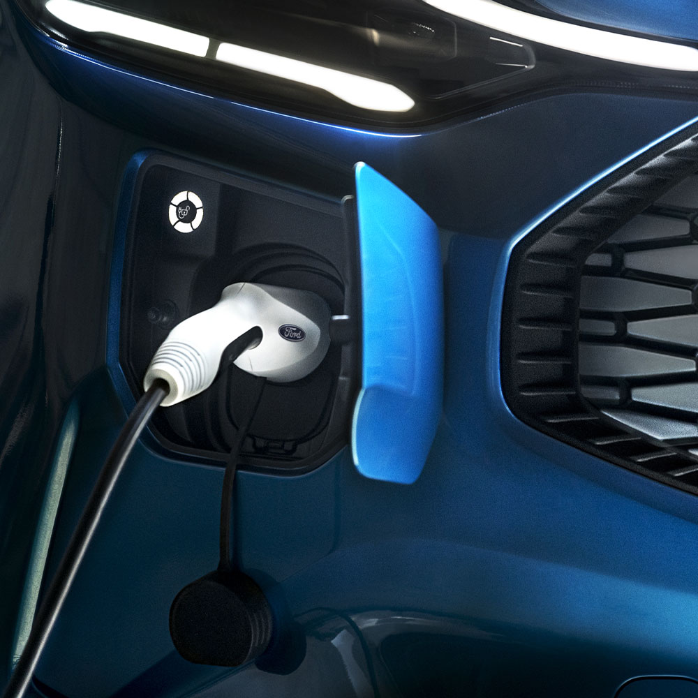 Nabíjecí port elektromobilu s připojenou nabíječkou elektromobilů naproti modrému vozidlu Ford.