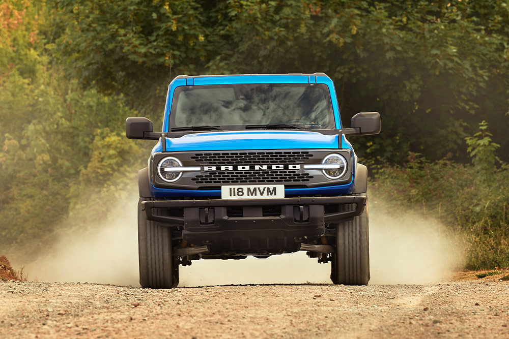 Pohled zepředu na modrý Ford Bronco, který jede po polní cestě.