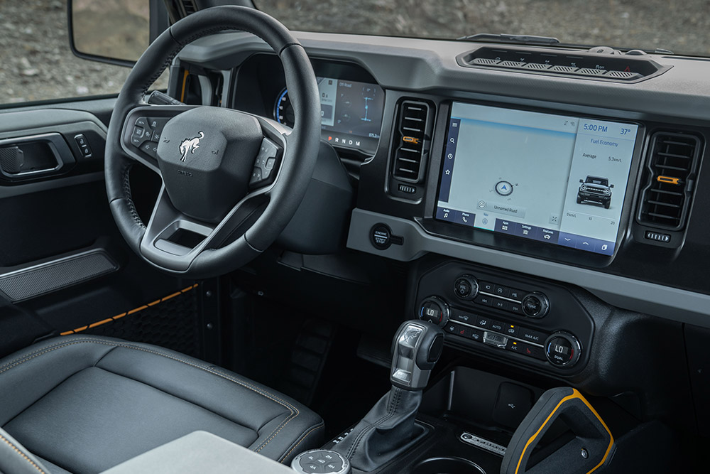 Pohled na interiér Fordu Bronco, včetně koženého volantu a připojeného touchpadu.