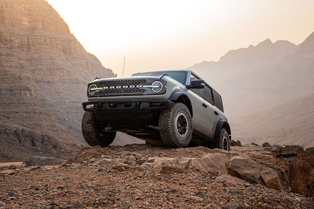 Šedý Ford Bronco stojí zaparkovaný na skalnaté cestě v horské krajině.