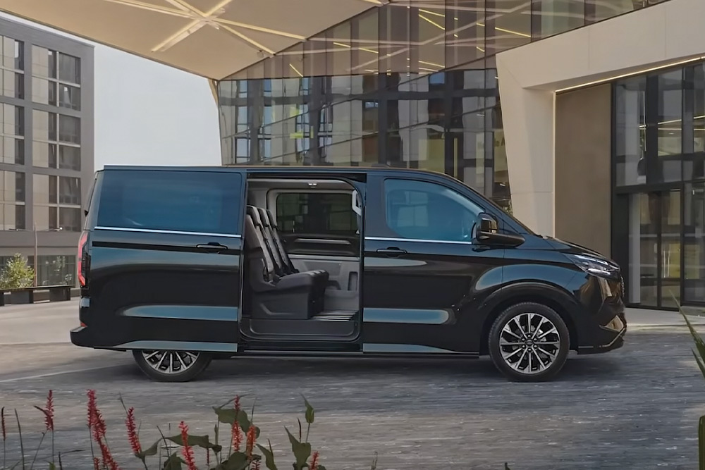 Černý Ford E-Tourneo Custom zaparkovaný s otevřenými bočními dveřmi odhalujícími sedadla interiéru.