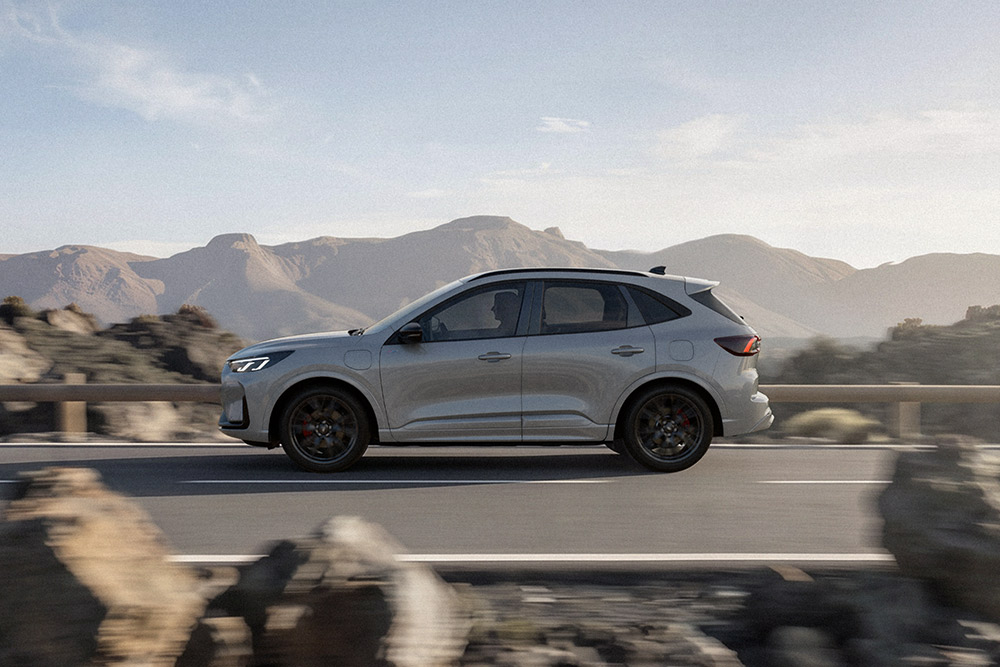 Stříbrný Ford Kuga projíždí malebnou horskou trasou. 