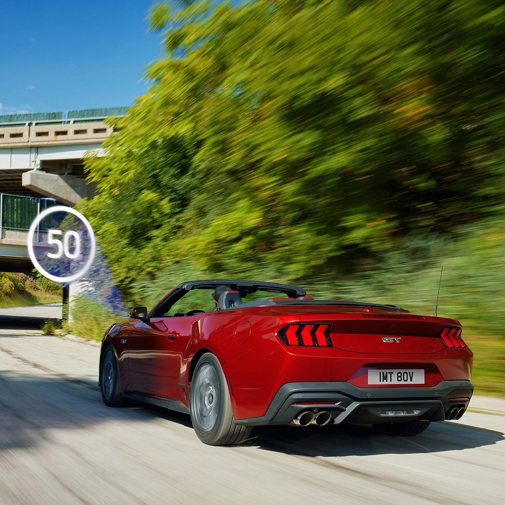 Červený Ford Mustang projíždějící okolo dopravní značky.