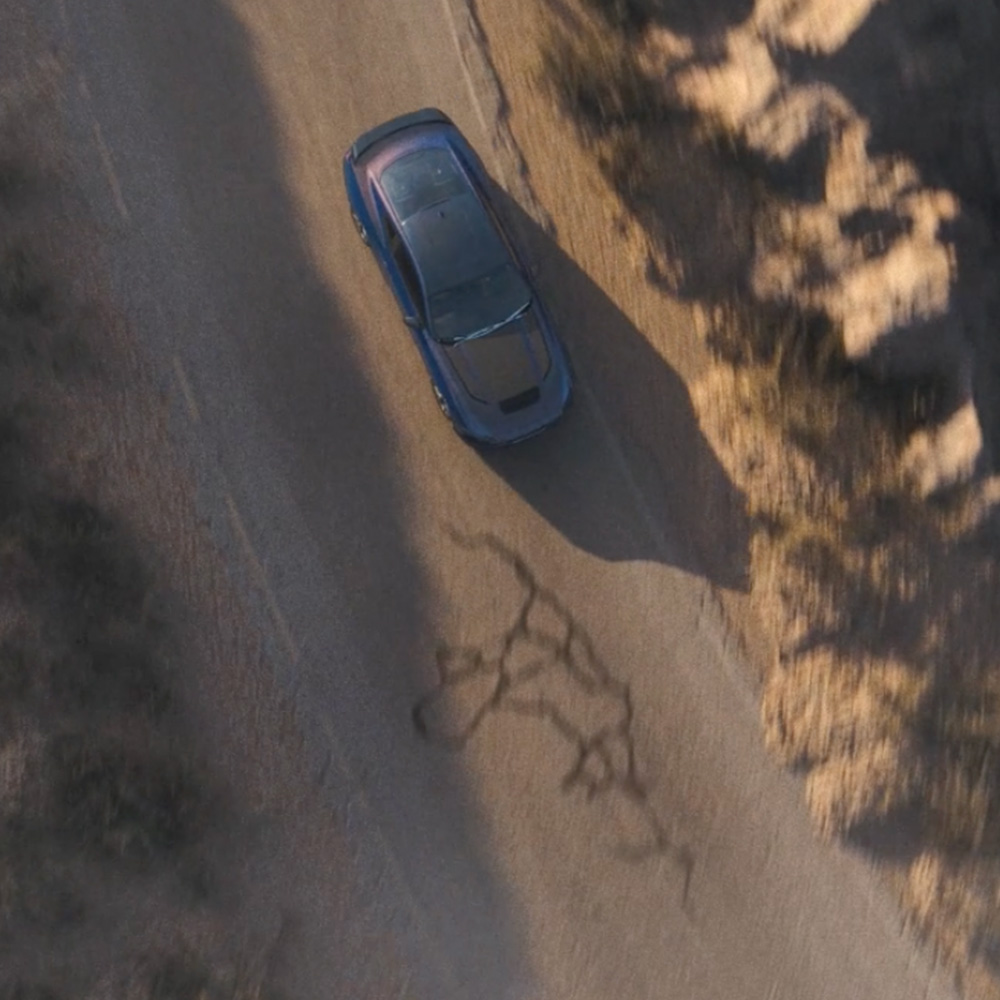 Pohled shora na Ford Mustang Dark Horse v modré Ember jedoucí po horské cestě.