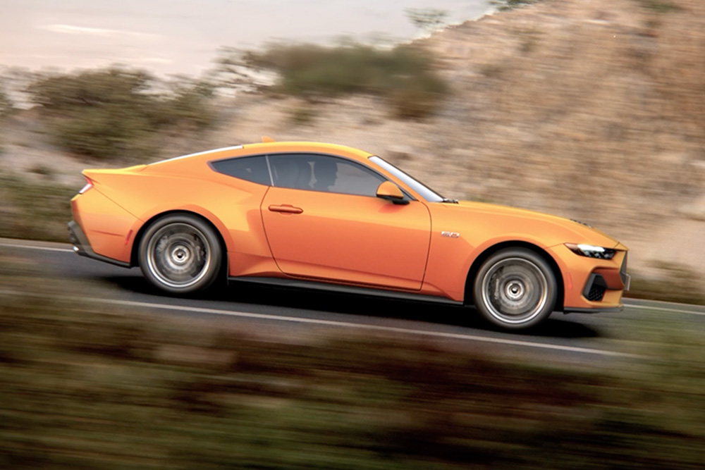 Boční pohled na Ford Mustang GT v oranžové Fury jedoucí po silnici.