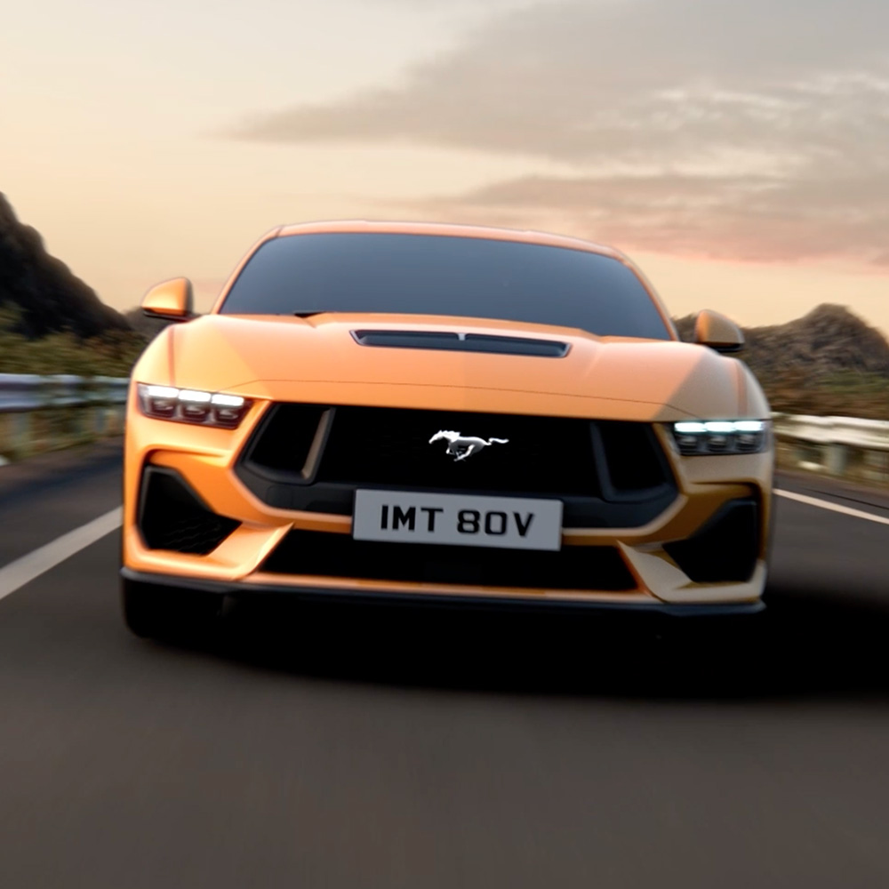 Přední pohled na oranžový Ford Mustang s detailním záběrem na světlomety, masku chladiče a znak Mustang.