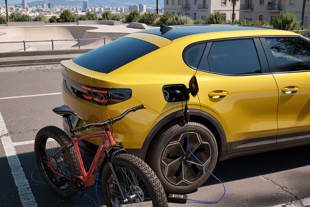 Žlutý Ford Capri® zaparkovaný v městské zástavbě při nabíjení červeného elektrokola