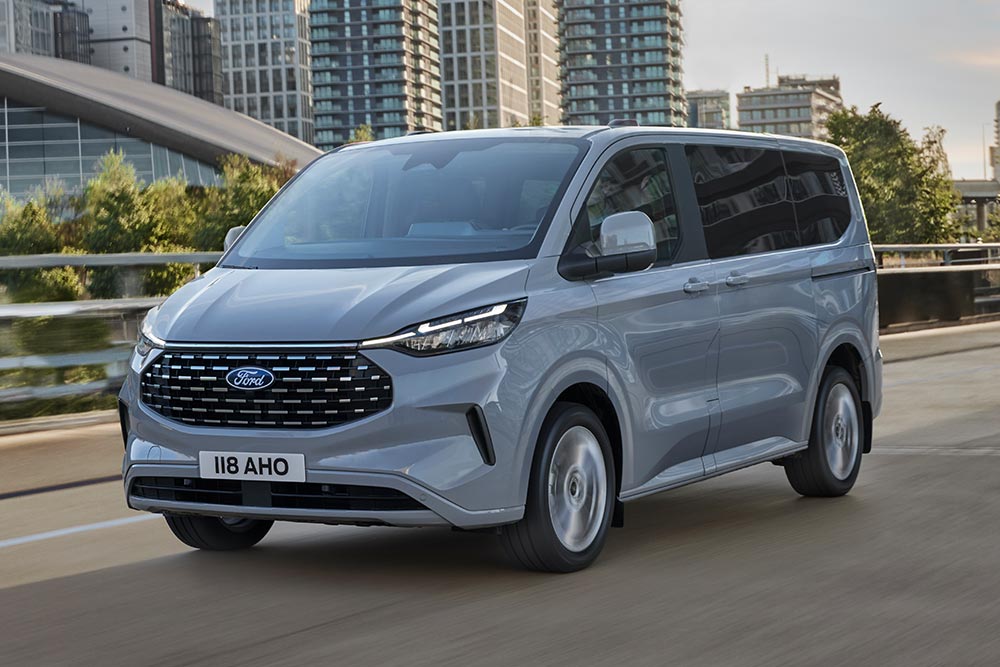 Šedé Ford Tourneo Custom jedoucí po městské silnici.