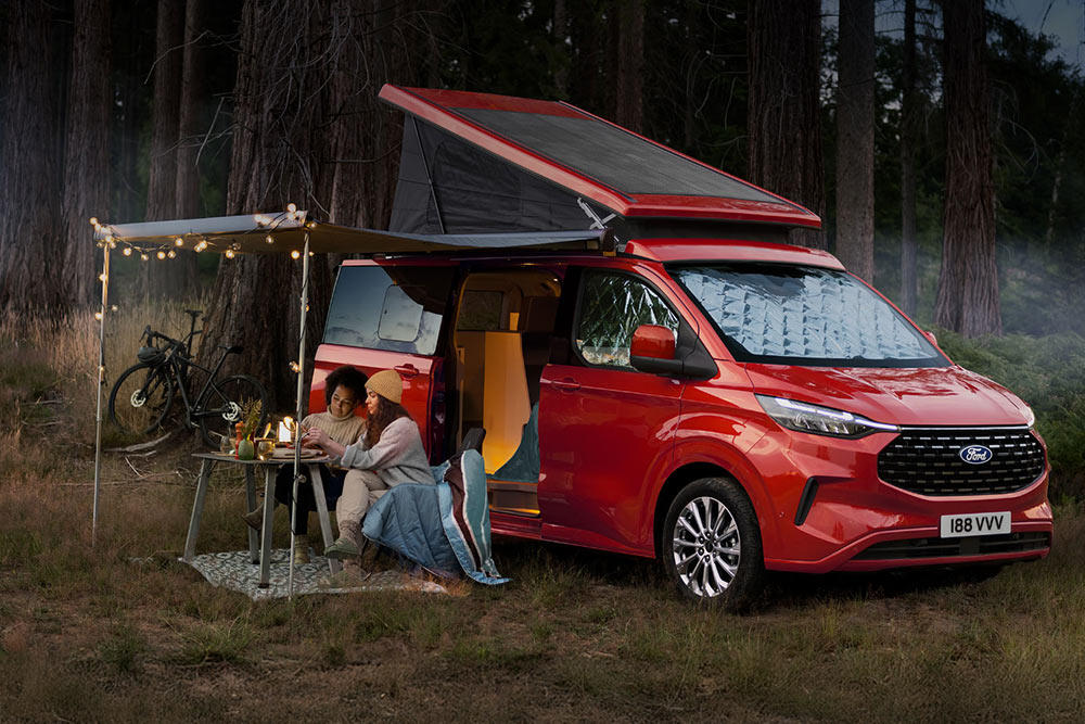Dvě ženy sedí pod markýzou u obytného vozu Ford Transit Nugget s otevřenou střechou.