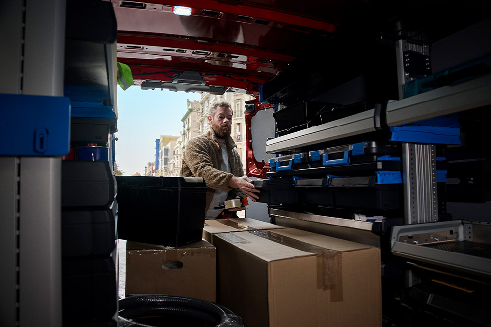 Kurýr vykládá balíky z červeného vozu Ford Transit Custom.