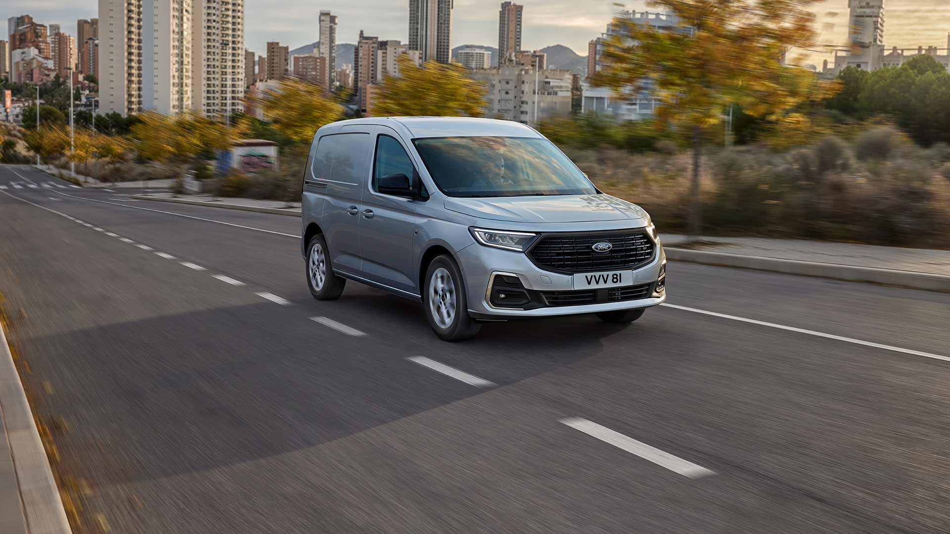 Ford Transit Connect s chromovanými exteriérovými mlhovými světlomety a automatickými světlomety projíždí městem.